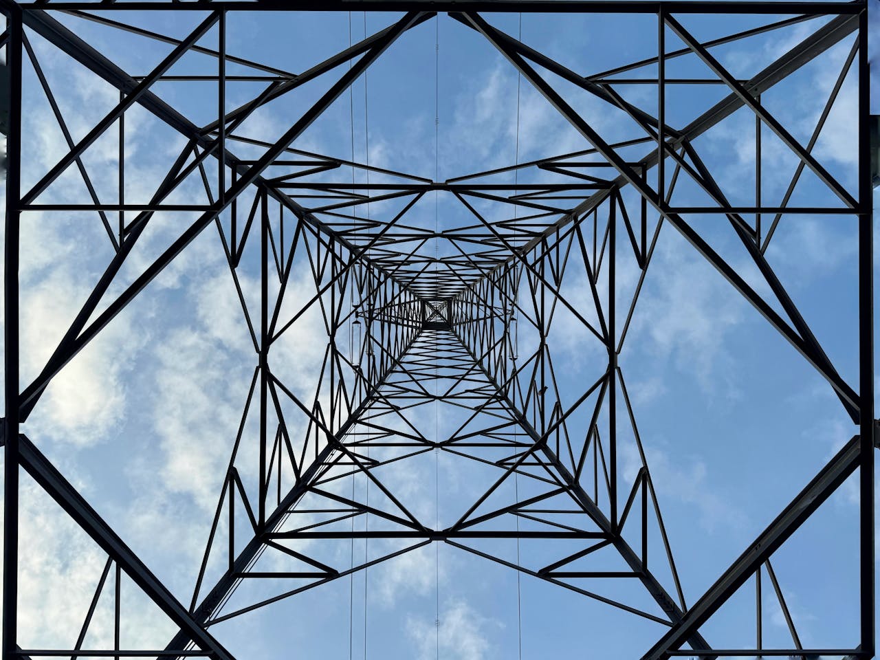 Looking up at the intricate geometry of a transmission tower against a clear blue sky.